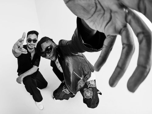 Black and white studio shot of two stylish adult men with sunglasses, posed with a hand reaching into the frame.