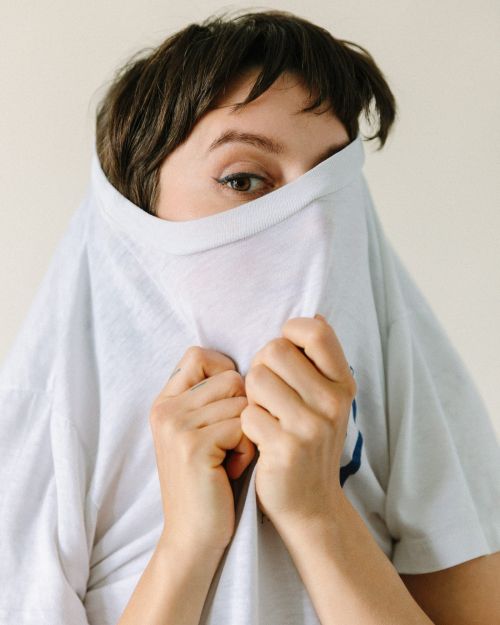 Close-up studio shot of a woman partially obscured by a white t-shirt, focusing on her eyes and the texture of the cotton fabric.