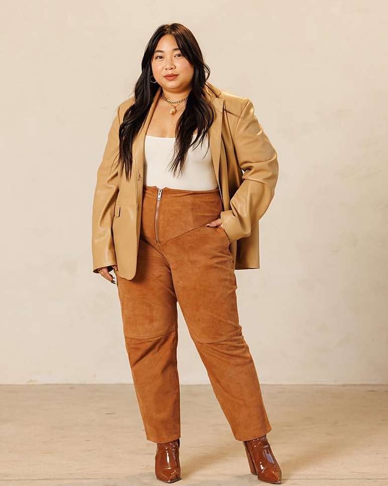 Adult woman in a tan leather blazer and brown pants poses in a studio. Neutral colors. Fashion editorial image. Lifestyle.