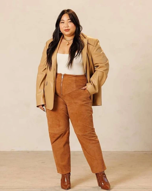 Adult woman in a tan leather blazer and brown pants poses in a studio. Neutral colors. Fashion editorial image. Lifestyle.