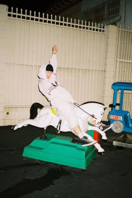 A person wearing a hooded jacket and black cap riding a white horse coin-operated machine with a blue machine in the background.