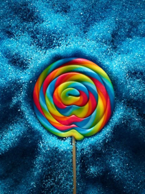 Close-up of a vibrant, swirled lollipop in a spiral design, surrounded by granulated, sparkling blue sugar, creating a colorful and sweet aesthetic.