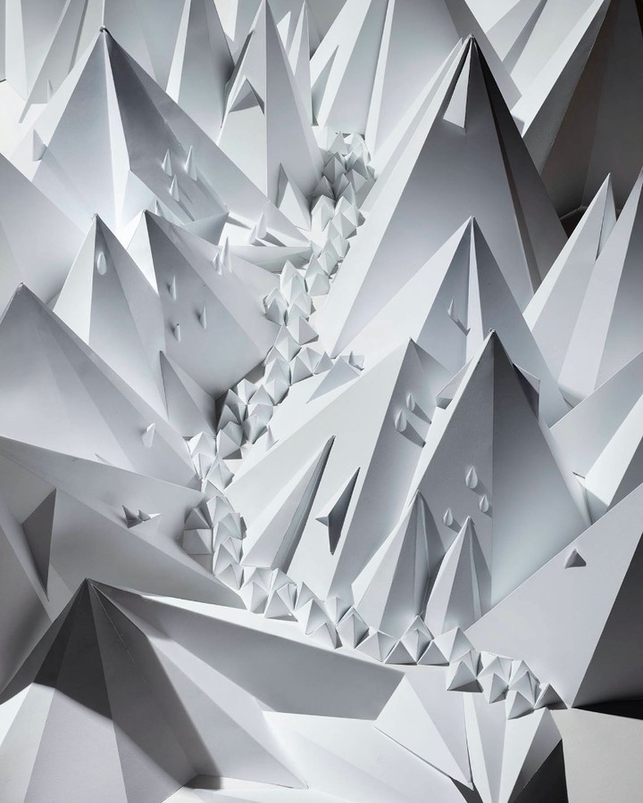 Paper art design featuring abstract geometric mountain peaks and river, creating a monochromatic landscape with shadows and depth.