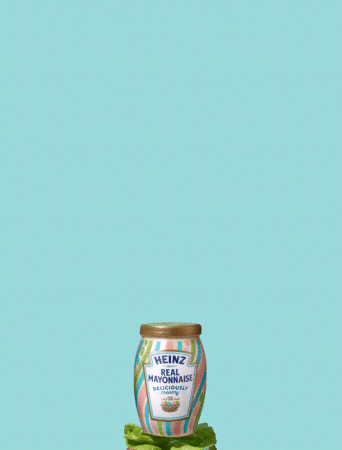 A jar of Heinz Real Mayonnaise with colorful stripes sits atop green lettuce against a solid light blue background.