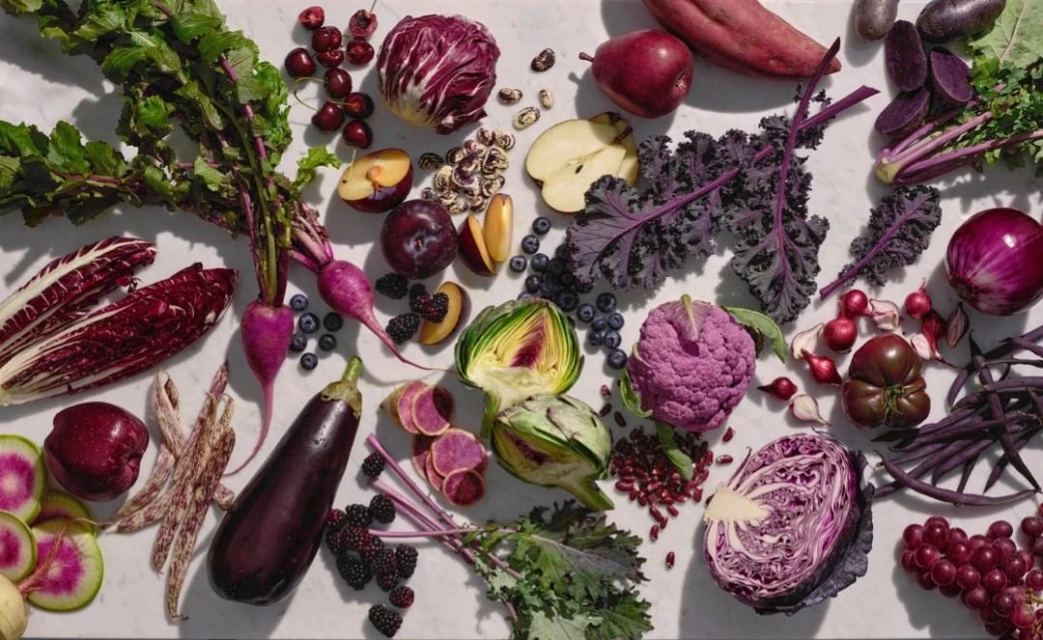 Overhead shot of purple produce including eggplants, cabbage, cauliflower, and radishes on a white marble surface.