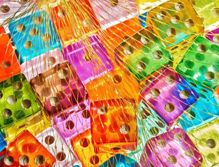 Close-up of a group of colorful dice in an orange mesh bag, displaying various numbers, creating a vibrant, playful aesthetic.