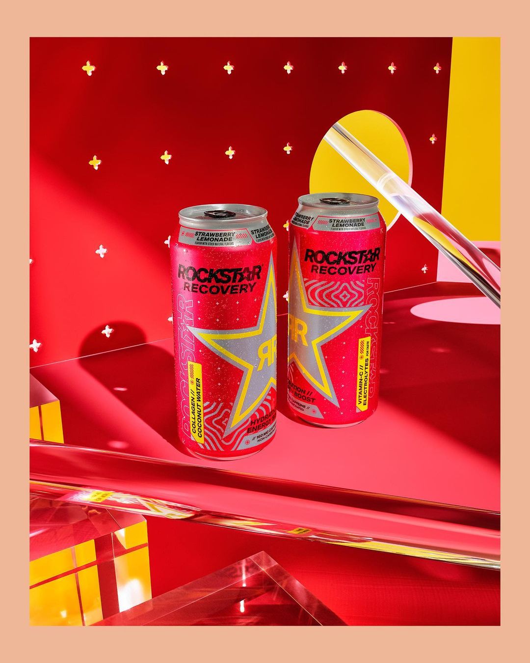 Two cans of Rockstar Recovery strawberry lemonade flavored drink on a red surface with geometric shapes and modern lighting.
