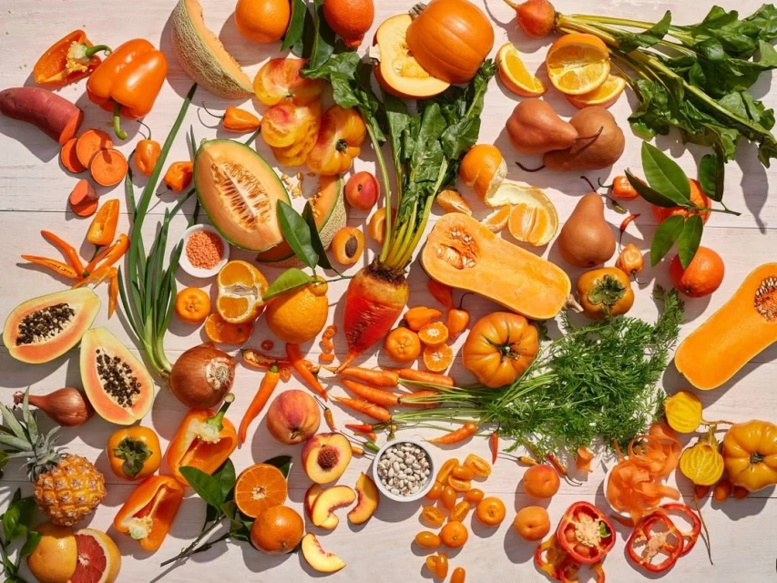 Overhead shot of various orange fruits and vegetables including citrus, squash, sweet potatoes, peppers, cantaloupe, and carrots.
