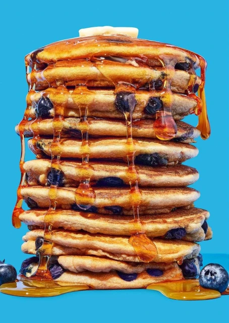 Stack of blueberry pancakes with butter and maple syrup against a blue background in a studio setting for a food photography shoot.