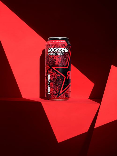Studio shot of a red can of Rockstar Punched fruit punch energy drink on a red surface with red shadows creating geometric patterns.
