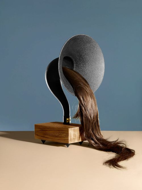 Artistic studio shot of a vintage gramophone with cascading brown hair emerging from the speaker, set against a blue backdrop.