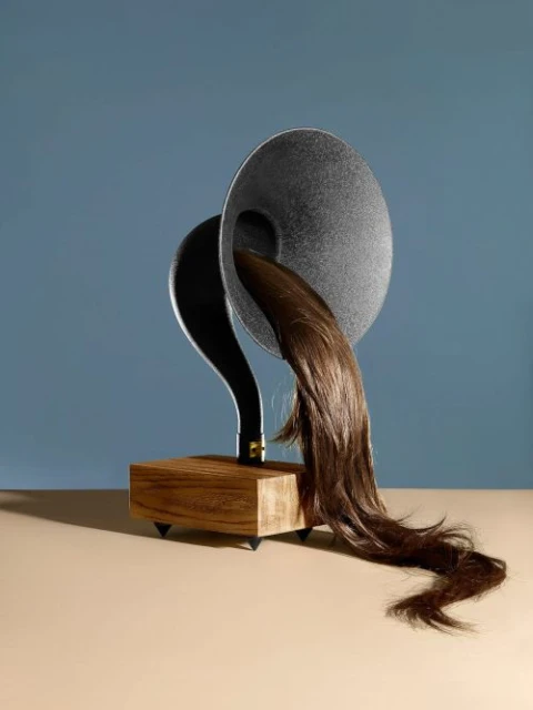 Artistic studio shot of a vintage gramophone with cascading brown hair emerging from the speaker, set against a blue backdrop.
