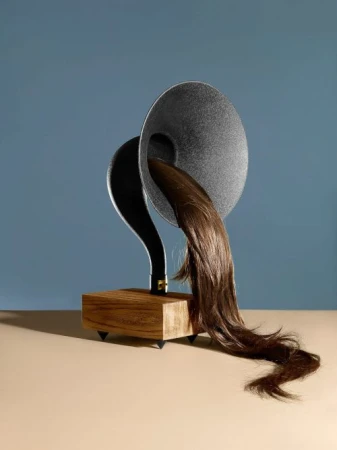 Artistic studio shot of a vintage gramophone with cascading brown hair emerging from the speaker, set against a blue backdrop.