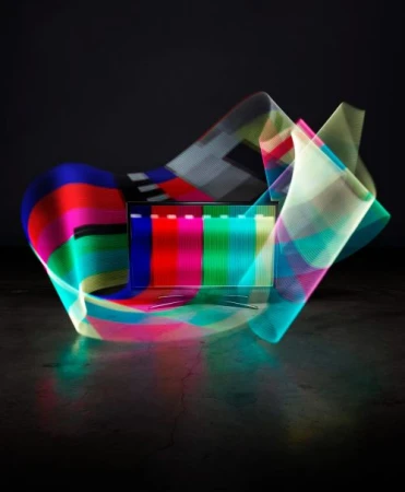 A colorful light painting effect showcases a laptop screen with a test pattern, set against a dark background, with light reflections.