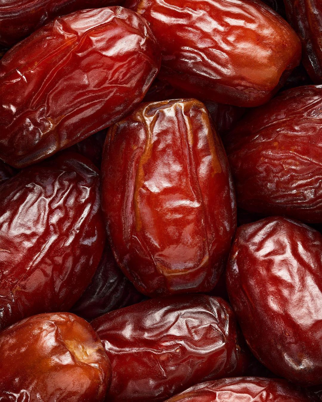 Close-up photo of many shiny brown dates, with visible wrinkled textures, highlighting their natural sweetness and inviting appearance.