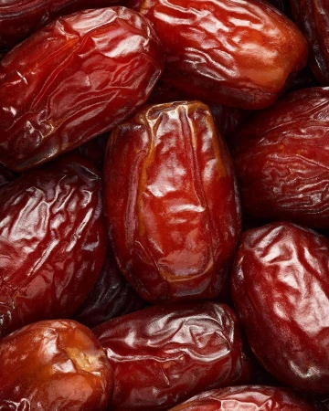 Close-up photo of many shiny brown dates, with visible wrinkled textures, highlighting their natural sweetness and inviting appearance.