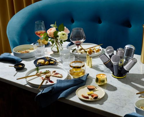Table setting with plates, glasses, flatware, flowers, and microphones suggesting a musical dining experience in a contemporary space.