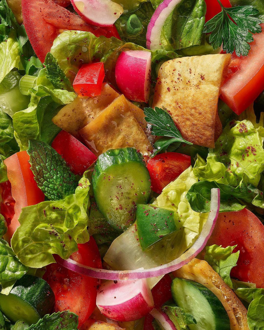 Overhead shot of a vibrant Fattoush salad featuring lettuce, tomatoes, cucumbers, radishes, onions, mint, parsley, and pita bread.
