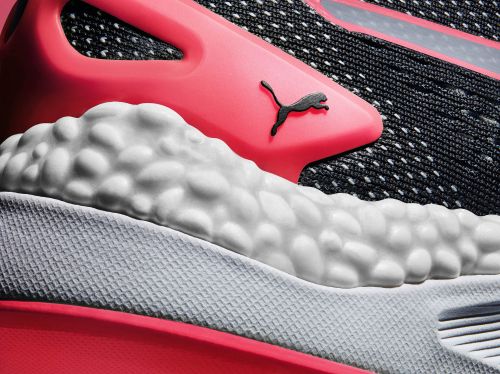 Close-up of a Puma running shoe with black patterned fabric, a coral-colored heel and upper, and a thick white textured sole.