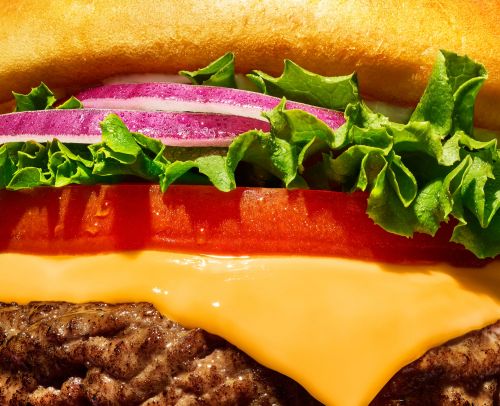 Close-up of a juicy hamburger with a beef patty, melted cheese, tomato, lettuce, and red onion on a toasted bun.