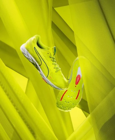 Neon yellow running shoes floating against a vibrant chartreuse draped fabric backdrop by The Voorhes