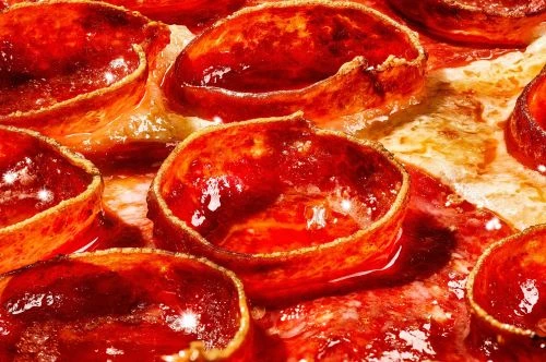 Macro photograph of a pepperoni pizza, showcasing the red, oily surface of the pepperoni and the melted cheese.