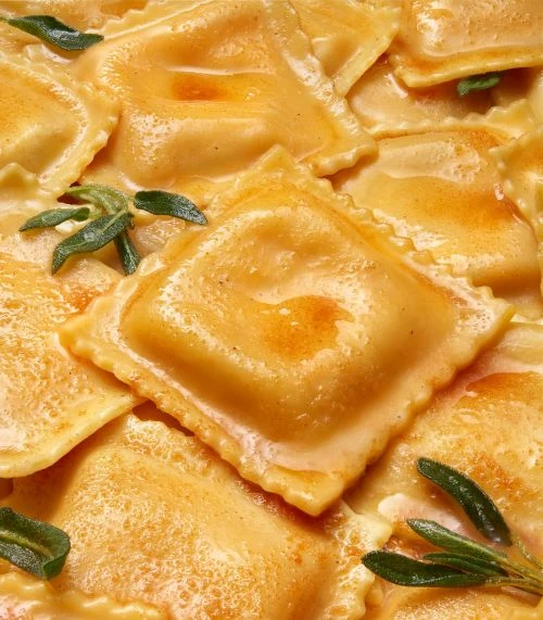 Overhead shot of cooked ravioli with a creamy sauce, garnished with green herbs. The pasta is golden, and sauce has a glossy finish.