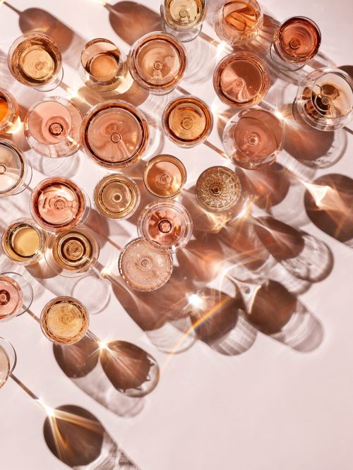 Overhead view of numerous glasses of wine casting sharp light refractions and long shadows on a white surface.