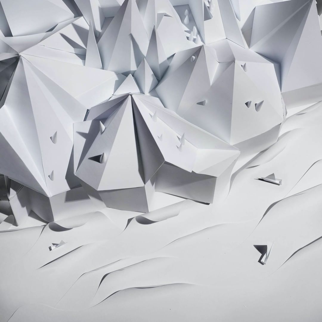 Abstract geometric paper art installation with triangular and pyramidal shapes in a monochromatic white color palette, minimalist design.