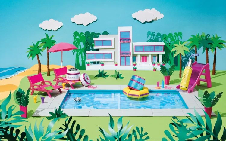 Paper art summer scene of pink lounge chairs near a pool with beauty products, palm trees, a modern house, and blue sky with clouds.