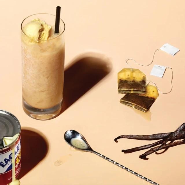 Iced tea beverage with ice cream, vanilla, and condensed milk on a neutral background. Tea bags and a long spoon are featured.