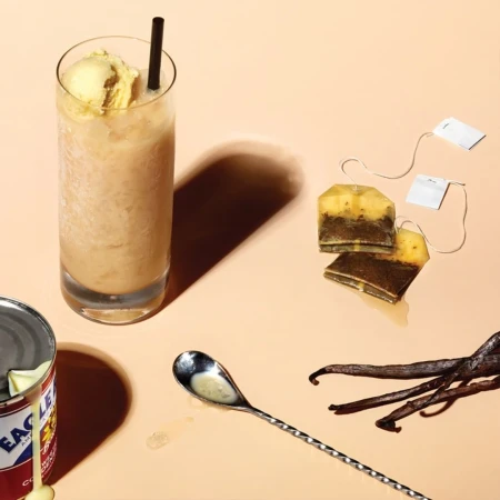 Iced tea beverage with ice cream, vanilla, and condensed milk on a neutral background. Tea bags and a long spoon are featured.