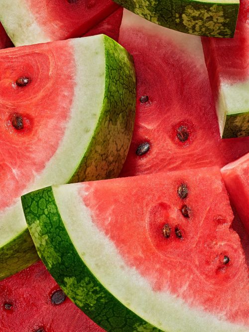 Close-up on vibrant watermelon slices revealing juicy red flesh and black seeds, contrasted by the rind's green hues and white edge.