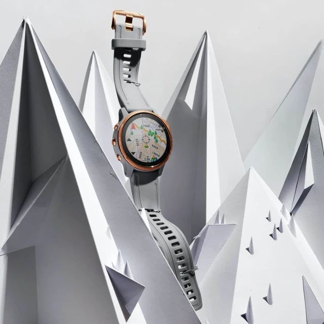 Smartwatch with grey band and rose-gold hardware is elevated against a white background of paper-folded origami mountains.