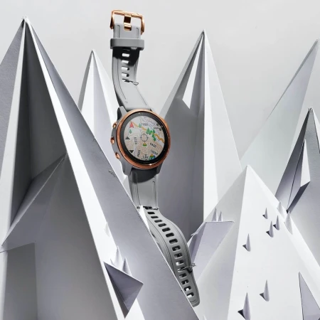 Smartwatch with grey band and rose-gold hardware is elevated against a white background of paper-folded origami mountains.