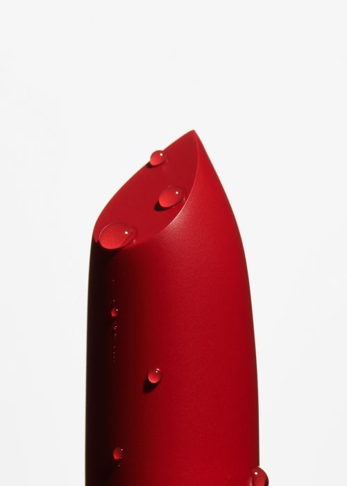 Close-up shot of a red lipstick with water droplets on a white background for beauty product photography and cosmetics advertising.