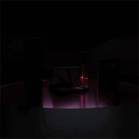 Dark product shot of an open laptop and glass against a black background with purple-pink light emitting below the objects.