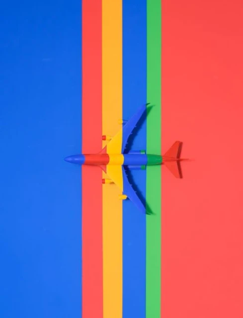 Overhead shot of toy airplane on colorful stripes: blue, yellow, green, and red. Vibrant, eye-catching abstract pattern.