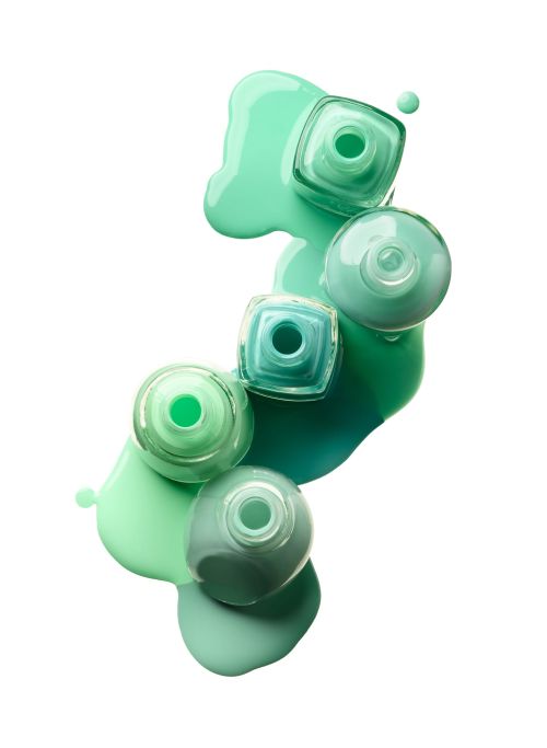 Overhead shot of multiple bottles of colorful nail polish with spilled product on a clean white surface, beauty product photography.
