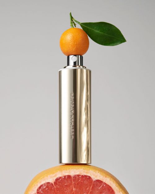 Still life of a perfume bottle with an orange and grapefruit against a grey background in a beauty and cosmetics product shot.