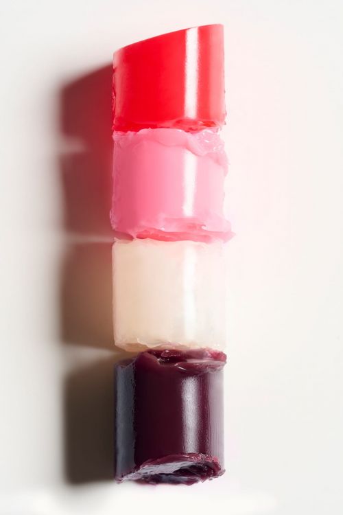 A stacked lipstick tower showcases shades of red, pink, white, and burgundy on a plain white surface in a beauty still life.