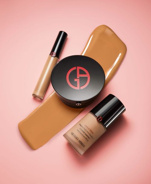 Giorgio Armani beauty products, including foundation and concealer, are presented on a light pink surface with a swatch of foundation.