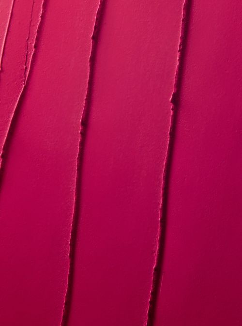 Close-up texture of bright pink lipstick or cosmetic cream, featuring vertical streaks and a smooth, vibrant surface.