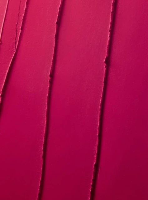 Close-up texture of bright pink lipstick or cosmetic cream, featuring vertical streaks and a smooth, vibrant surface.