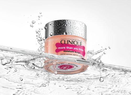 Clinique Moisture Surge jar stands in splashing water, creating a fresh and hydrating image. The jar's label and water droplets emphasize moisture.
