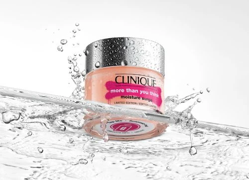 Clinique Moisture Surge jar stands in splashing water, creating a fresh and hydrating image. The jar's label and water droplets emphasize moisture.