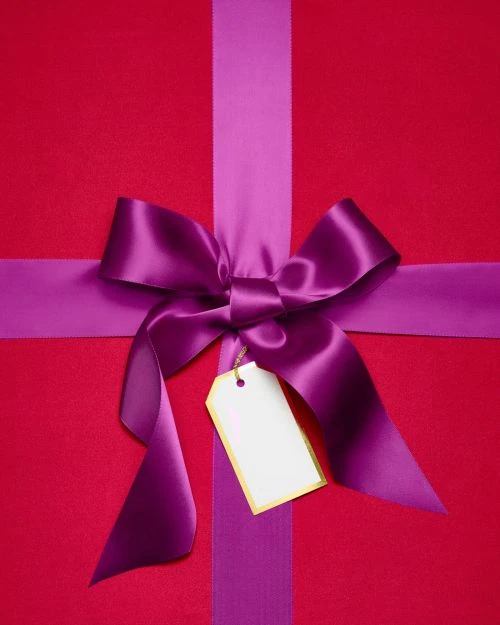 A close-up of a red gift box decorated with a purple ribbon and a blank white gift tag, creating a festive and celebratory image.