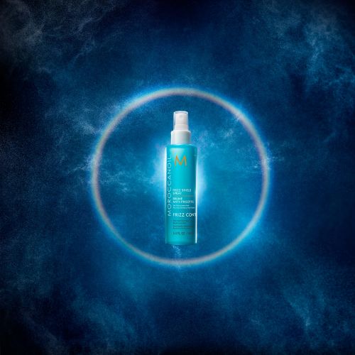 Turquoise spray bottle of Moroccanoil Frizz Control hair product on a dark blue background with a glowing circle around the product.
