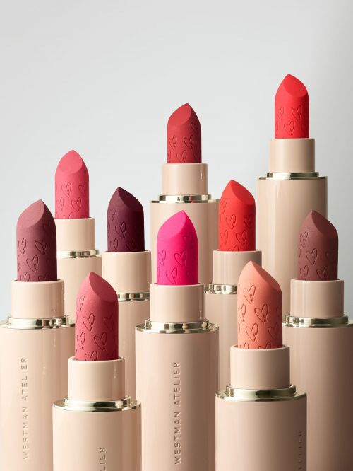 Multiple tubes of Westman Atelier lipsticks in various colors, arranged in a staggered, elevated display on a white backdrop.