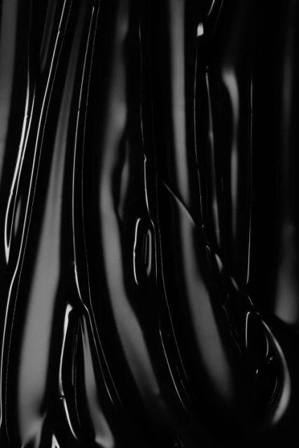 Abstract close-up of shiny black liquid forming rippled, glossy patterns, creating a dark and textured monochrome effect with highlights.